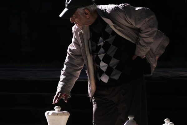 man in black and white jacket and black pants standing beside white chess piece